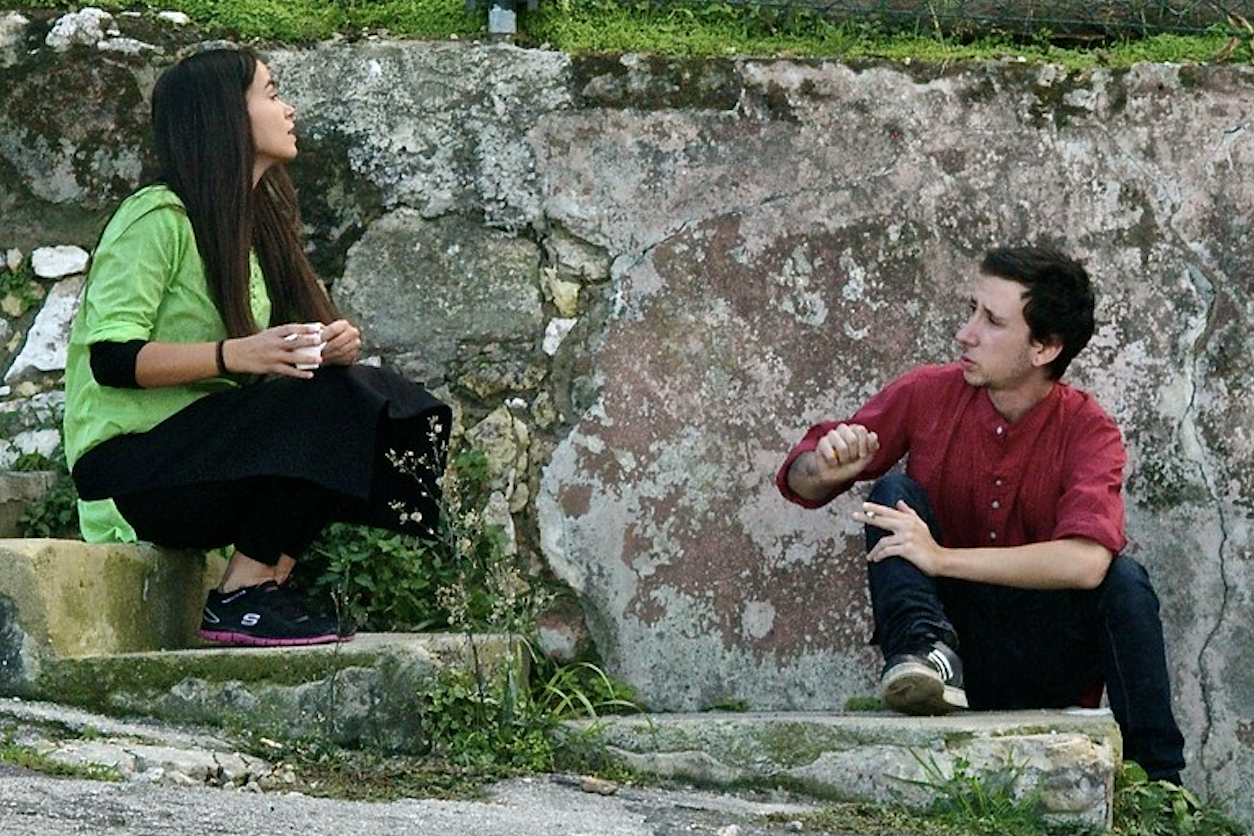 a man and a woman speak informally sitting on steps.