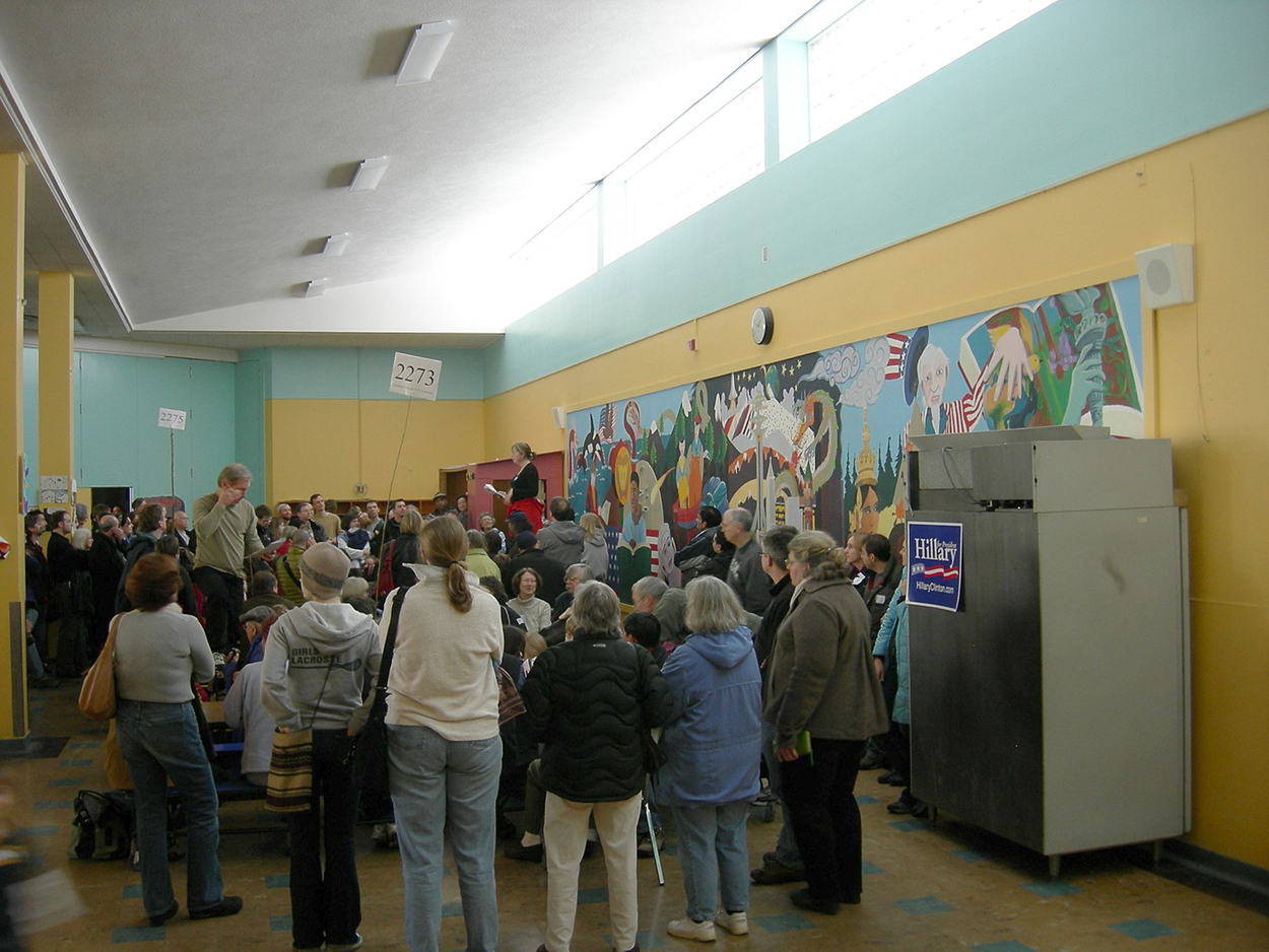 (Figure 4) Caucus-goers gather at a Democratic precinct caucus on January 3, 2008, in Iowa City, Iowa. Caucuses are held every two years in more than 1,650 Iowa precincts. People gathered in a hall listening and signing sheets.