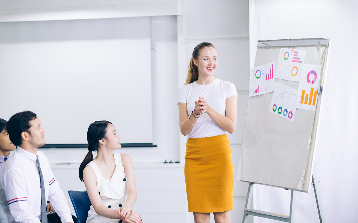 A woman gives a speech with the help of graphs and charts on a board as visual aids.