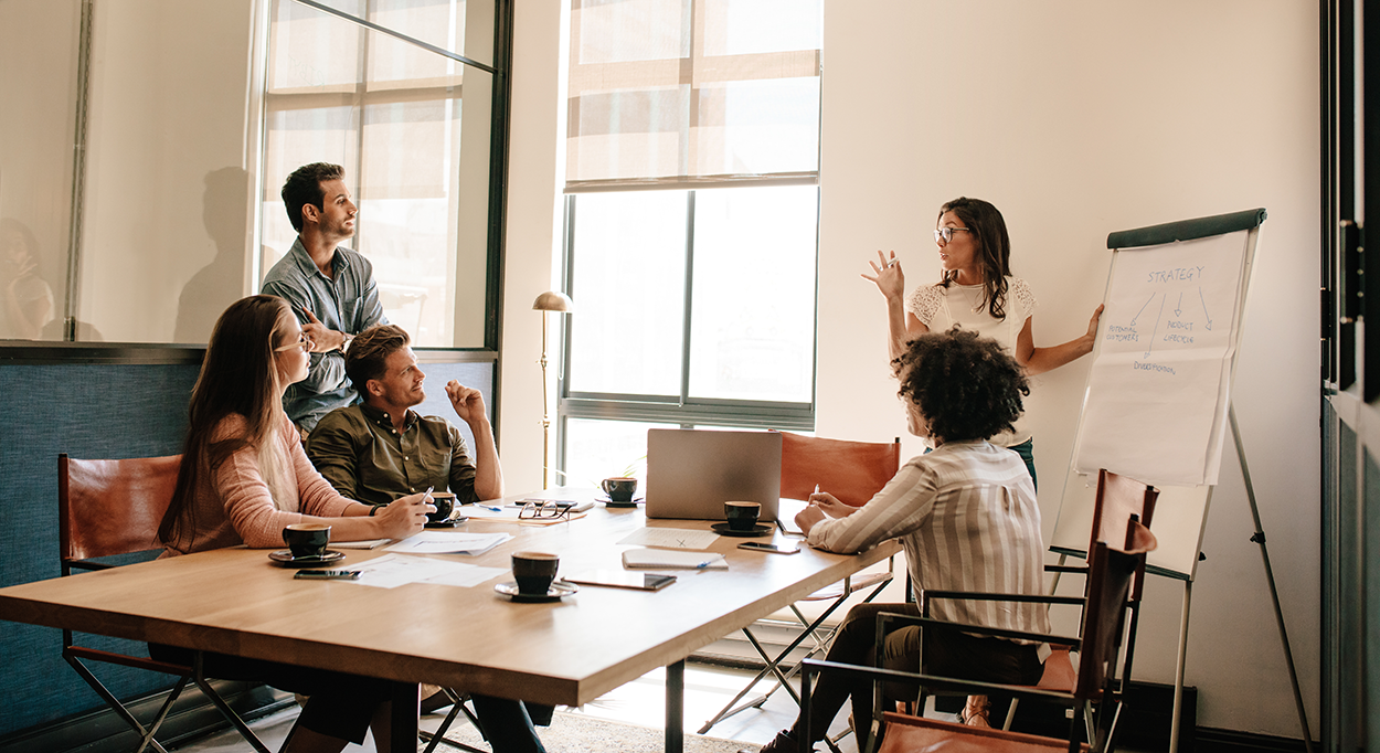 A woman uses a flip chart to present to a small group in a business setting.