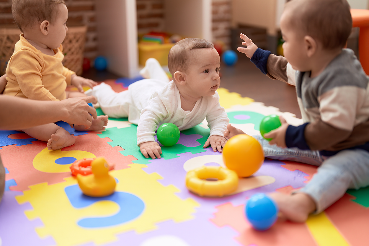 Image of babies playing on a play matt with toys. One baby is on their stomach while the other two babies are sitting.
