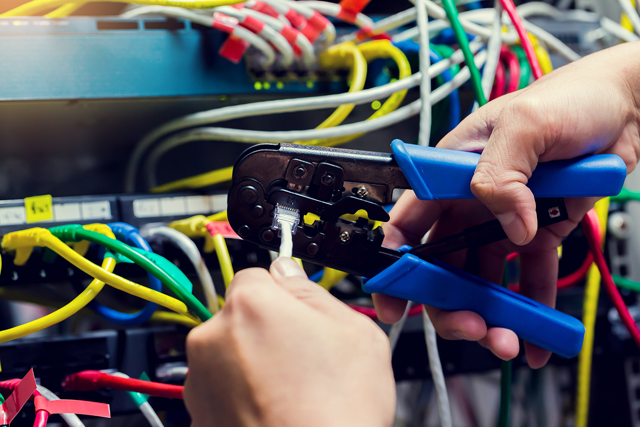 The process of crimping an Ethernet cable using a crimper tool. The tool has a metal body featuring notches and a blade, plus two handles for a comfortable grip and added leverage, making it simple to apply the pressure needed to secure the connector onto the cable.