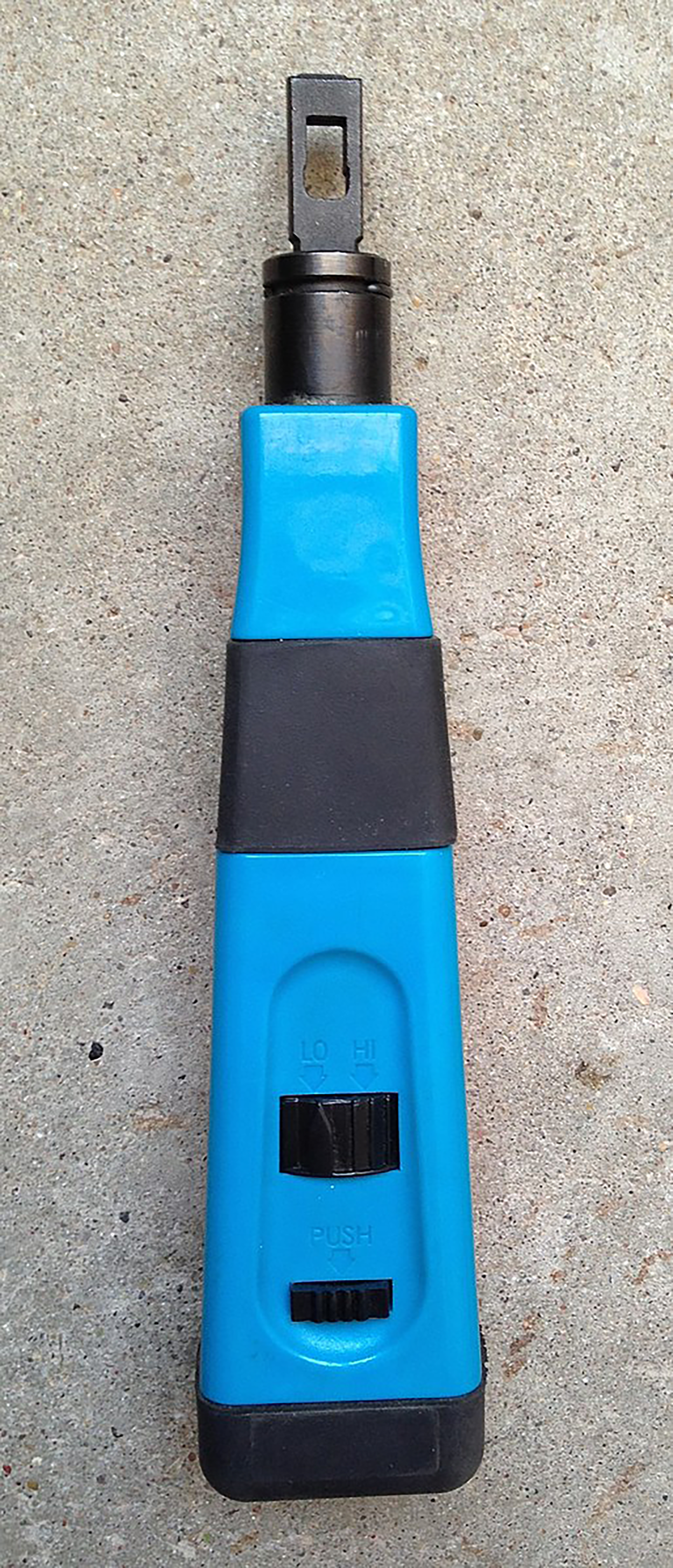 A punch-down tool with a plastic handle, featuring three black switches labeled ‘LO’, ‘HI’, and ‘PUSH’ to adjust the impact force. The top end has a metal blade designed for inserting and trimming wires into terminal blocks. The handle is wider at the base and gradually narrows toward the blade end.