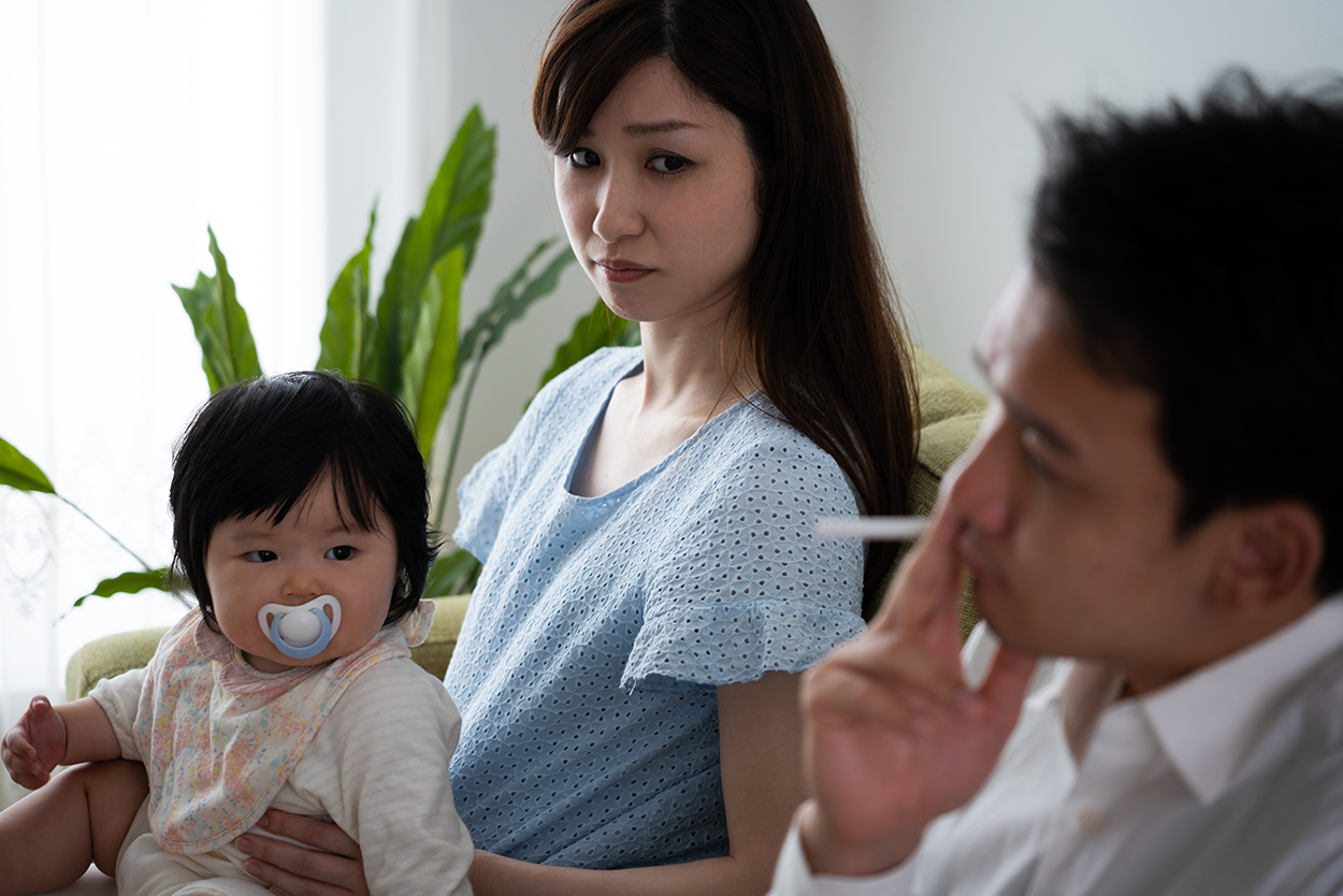 Shows a man smoking on a couch near a woman with a baby sitting on her lap. The woman and baby look concerningly at the man.