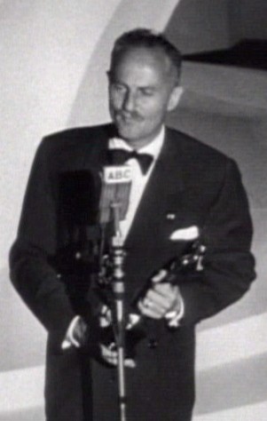 Darryl Zanuck, an American film producer and studio executive, accepts an Academy Award for Best Picture in 1947 for the film <i>Gentleman's Agreement</i>. A man in a suit holding an award statuette stands at a podium delivering an acceptance speech.