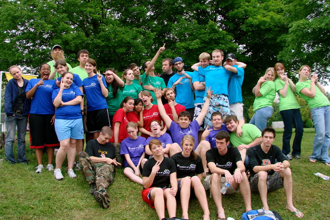 A group of young people smiling at the camera in multicolored t-shirts.