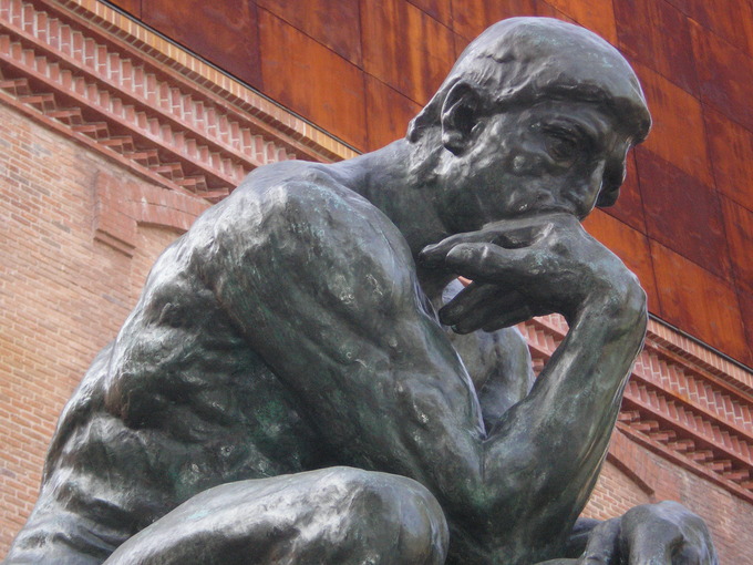 A statue of a man sitting down with his hand positioned below his chin in a thinking stance.