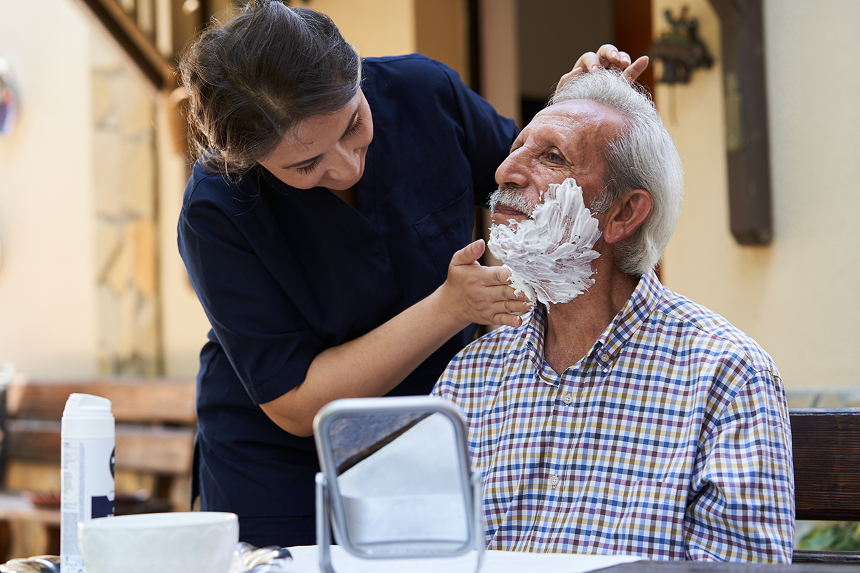 A caregiver helping a senior man shave during a home visit.