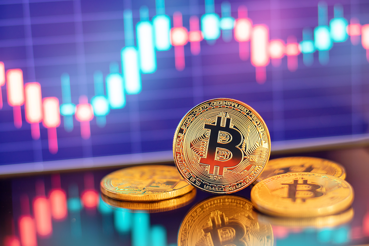 The image showcases a physical representation of Bitcoin placed on a reflective surface with a background featuring a digital candlestick chart. This visual symbolizes the volatility and market dynamics of cryptocurrency trading. Bitcoin, the first and most well-known cryptocurrency, operates on a decentralized blockchain network and is often used as a store of value or investment asset. The fluctuating chart in the background highlights the price movements characteristic of digital asset markets, emphasizing the speculative nature of Bitcoin investments.