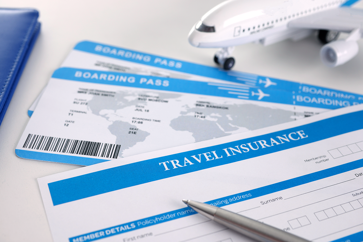 A travel insurance form with a pen resting on it, alongside two boarding passes and a small model airplane, representing travel planning and financial protection.