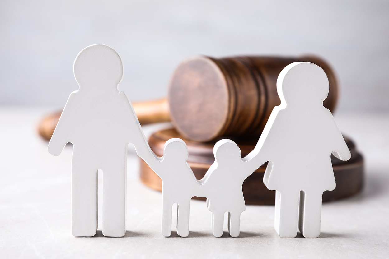 A wooden gavel in the background with a cutout figure of a family in the foreground, symbolizing legal matters related to family law, custody, or estate planning.
