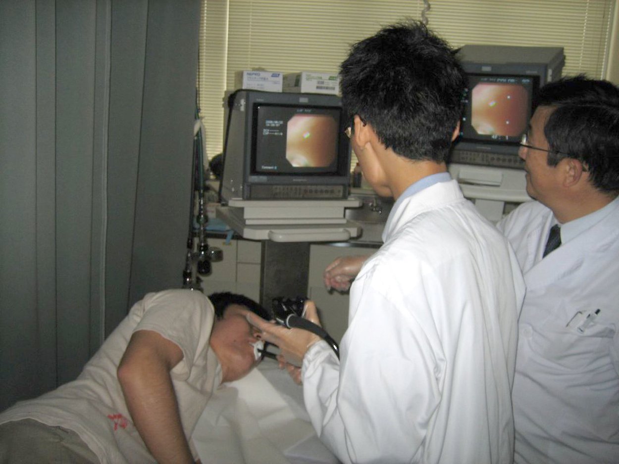 A patient lies on her side as doctors in white coats view a screen showing a picture from an endoscope. The endoscope has been placed through her mouth into her esophagus.