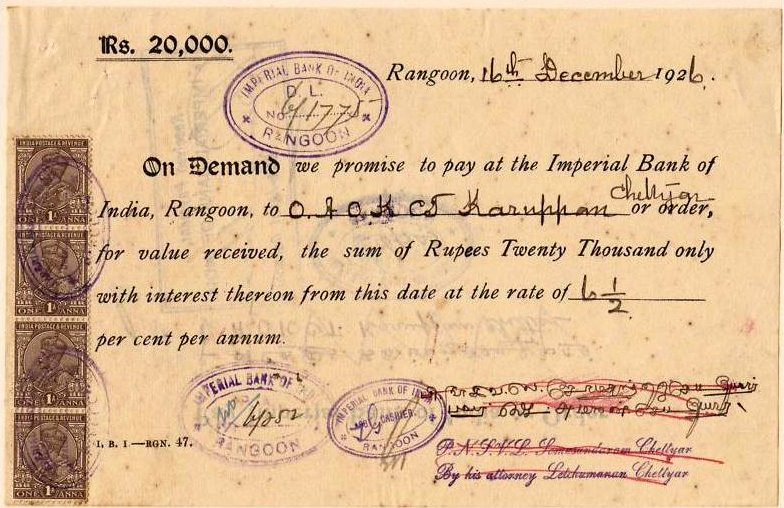 An old promissory note dated 1st December 1926, issued in Rangoon for Rupees 20,000. The note promises payment to the Imperial Bank of India, Rangoon, with interest at a specified rate per annum. It is handwritten with printed text, bearing several official stamps, seals, and signatures. The left margin features a vertical strip of revenue stamps. Ink stamps and handwritten entries are visible across the page.