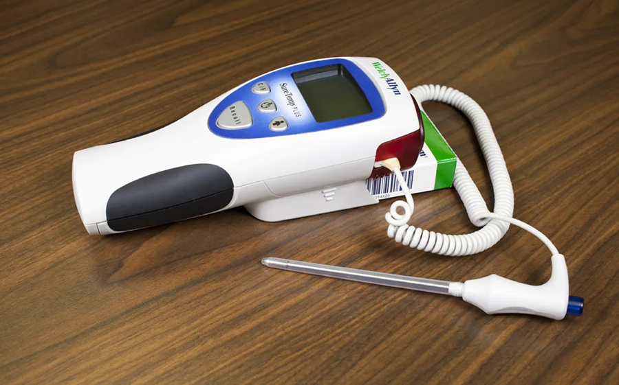 A photo of a narrow rectal thermometer attached by a wire to a device to display a reading. The device has a red color along the top side.