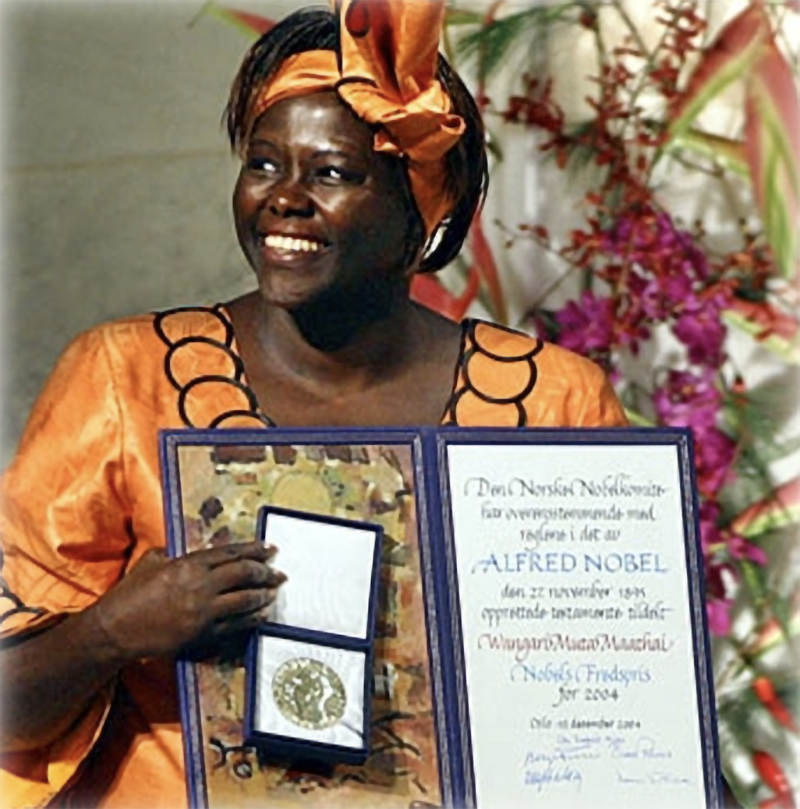 A smiling, dark skinned woman dressed in orange clothes and accessories holds up her Nobel Peace Prize Award and documents
