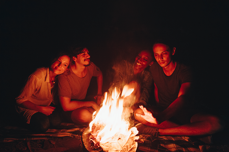 a group of people sitting outside around a fire of logs burning in a pit in the middle