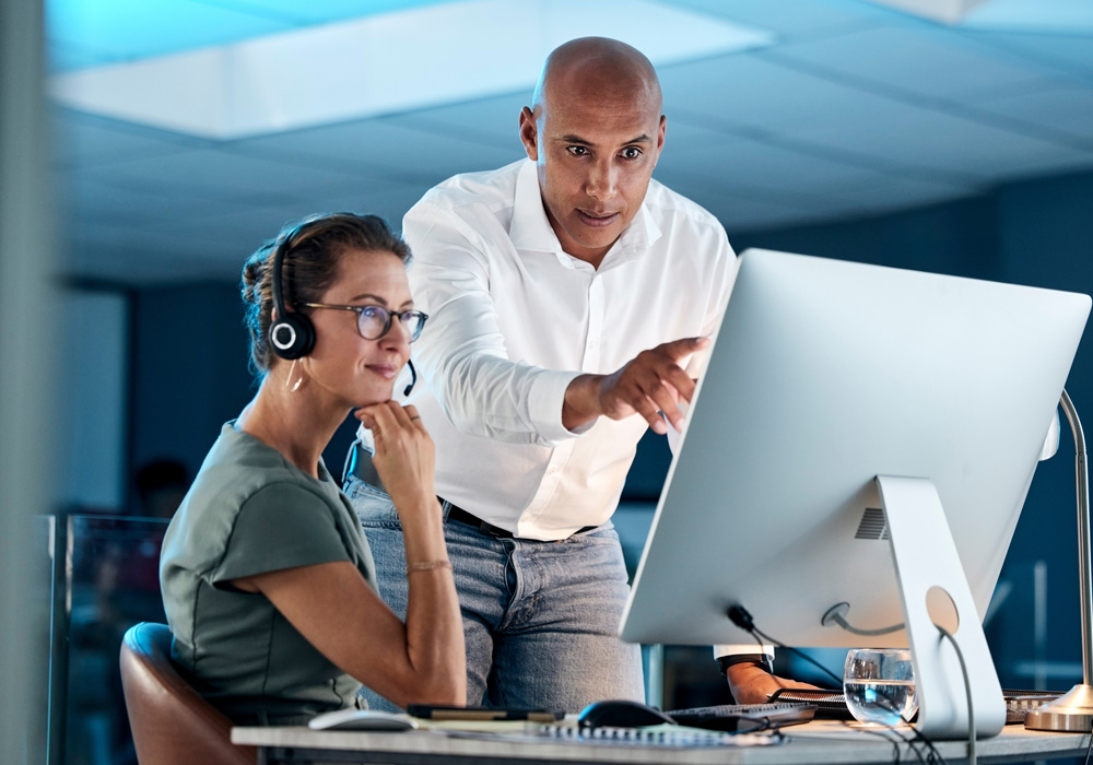 Two colleagues smiling and discussing something on a computer screen in a bright, modern office setting