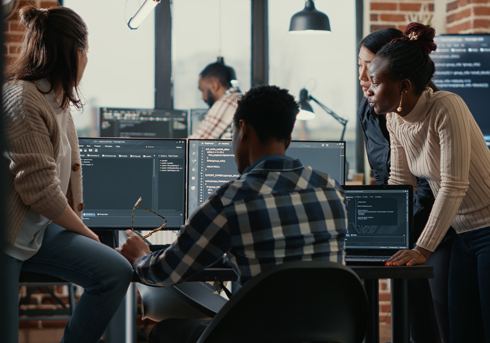 Group of professionals in a modern office discussing code displayed on a computer monitor during a software development meeting