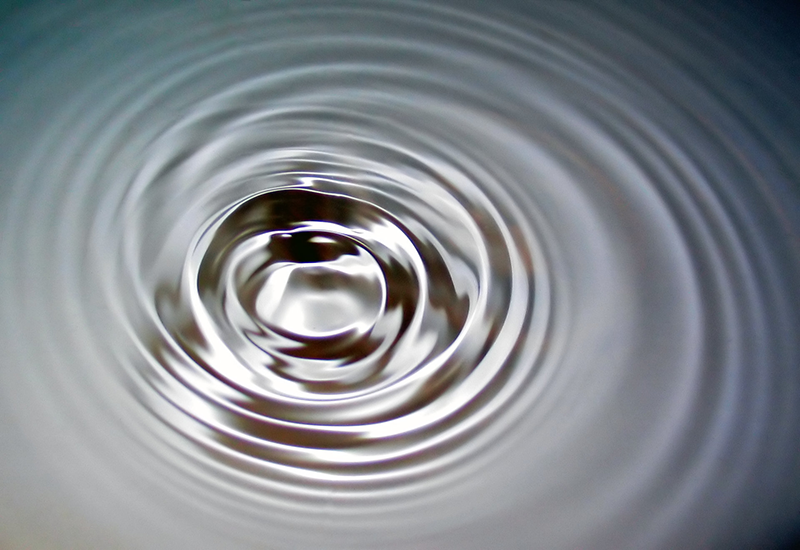 A silvery photo of circular ripples spreading outwards from the center against a dark backdrop