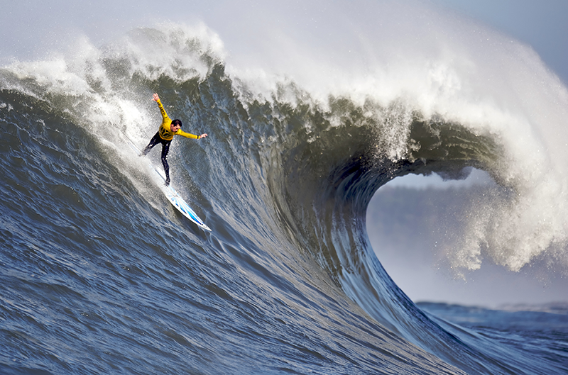 A surfer on a board rides on a large wave that is beginning to curl over