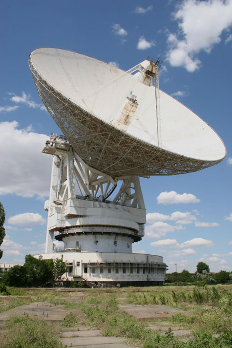 a very large, white, radio telescope outside in a field set against a blue sky
