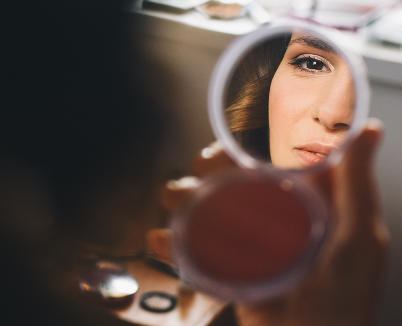 someone applying makeup in the magnifying side of a makeup mirror