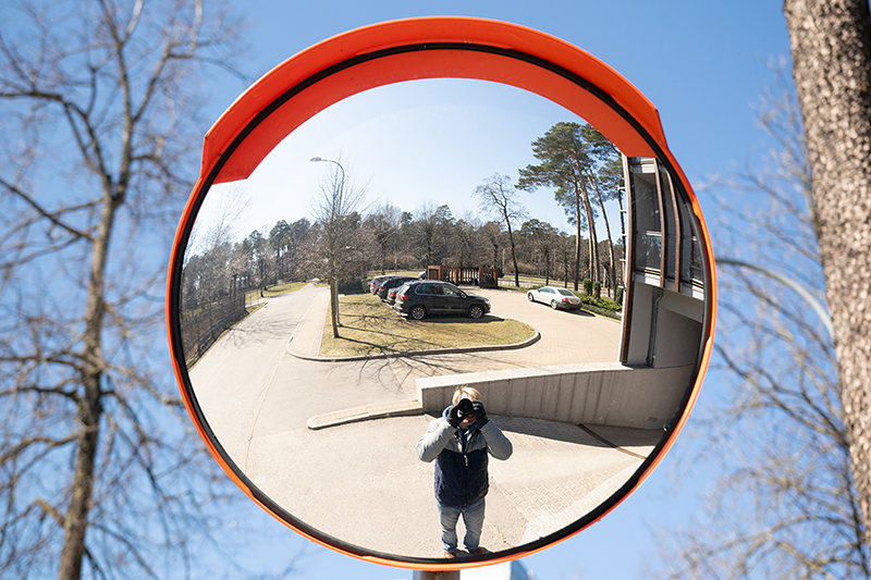 a convex mirror curving outward, showing a wide reflection of a person standing in front of it.